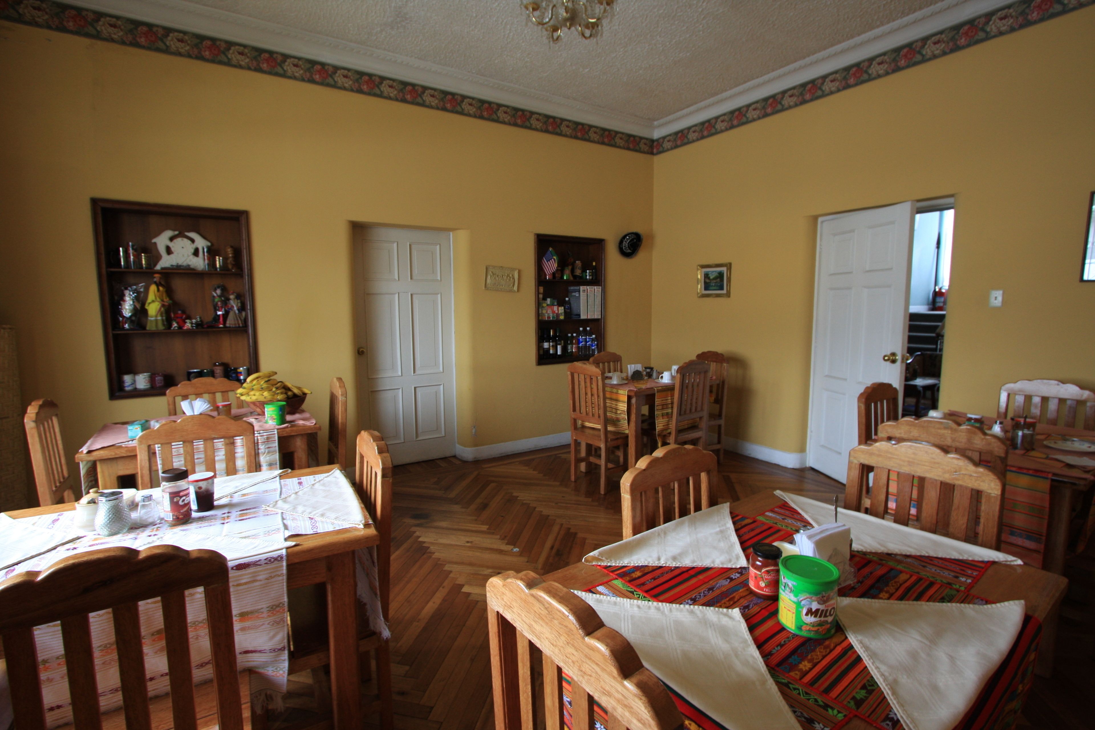 Comedor con sillas y mesas de madera, una estantería y una puerta que da a otra habitación.