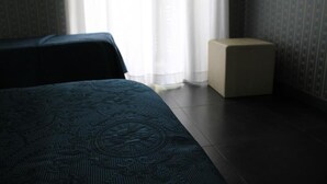 A hotel room with a bed, a small bedside table, and a window with curtains. - Hotel Guiren (Naples)