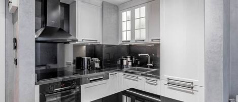 A modern kitchen with black countertops, stainless steel appliances, and white cabinetry.