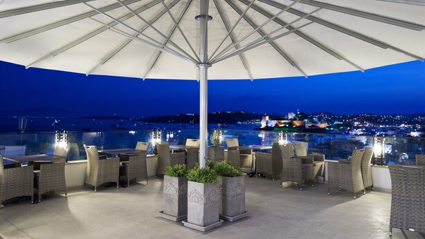 Una terraza al aire libre con un gran paraguas, muebles de mimbre y plantas en macetas.