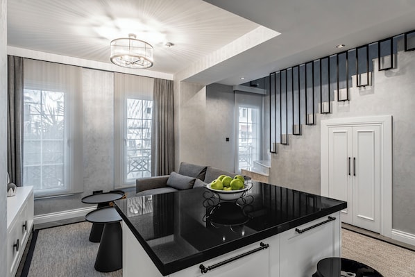 A modern kitchen with a black countertop, white cabinets, and a bowl of green apples.