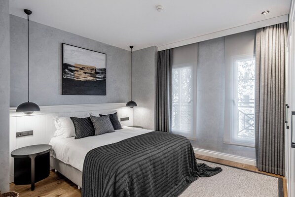 A modern bedroom with a large bed, two bedside lamps, a framed artwork, and a view of the outdoors through a window with curtains. - Ena Boutique Hotel & Residences (Bodrum)