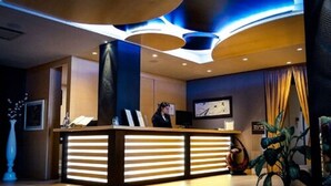 A reception desk with a modern design, a receptionist, and a large plant. - Modica Palace Hotel (Modica)