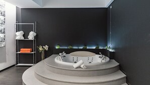 A modern bathroom with a freestanding bathtub, a towel rack with towels, and a shelf with toiletries. - Modica Palace Hotel (Modica)