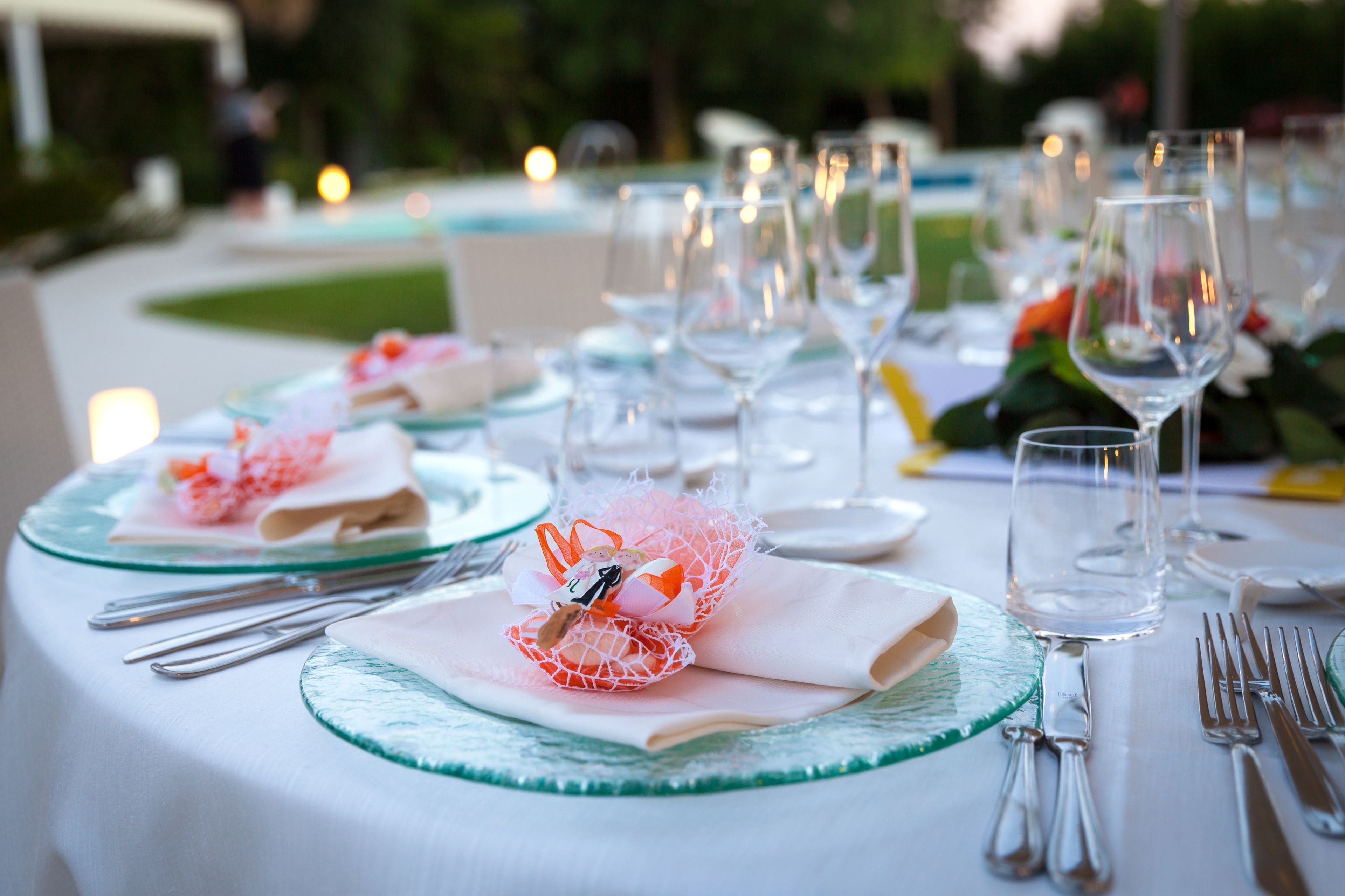 Mesa lista para un evento de cena al aire libre con vajilla de vidrio, servilletas dobladas y plato de vidrio.
