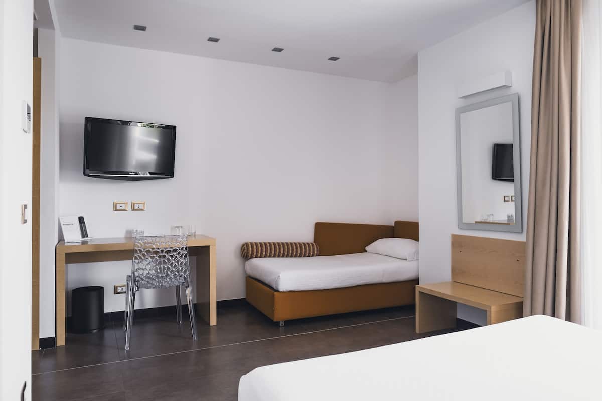 A hotel room with a bed, a desk with a chair, a TV mounted on the wall, and a mirror.