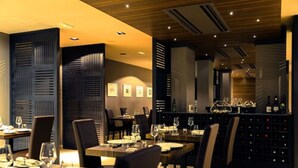 A restaurant with tables set for dining, a bar area with wine bottles, and framed pictures on the wall. - Modica Palace Hotel (Modica)