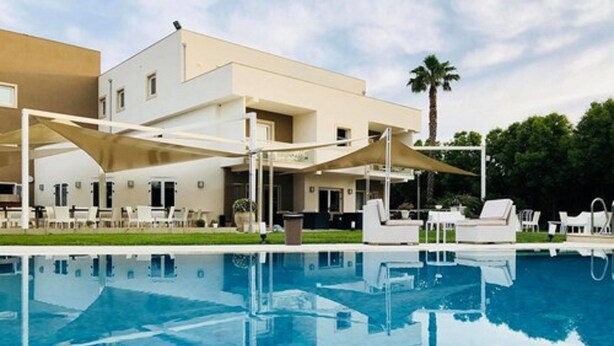 A modern hotel with a swimming pool, outdoor seating, and a palm tree in the background. - Modica Palace Hotel (Modica)