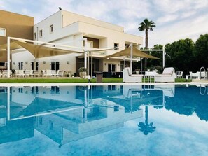 A modern hotel with a swimming pool, outdoor seating, and a palm tree in the background. - Modica Palace Hotel (Modica)