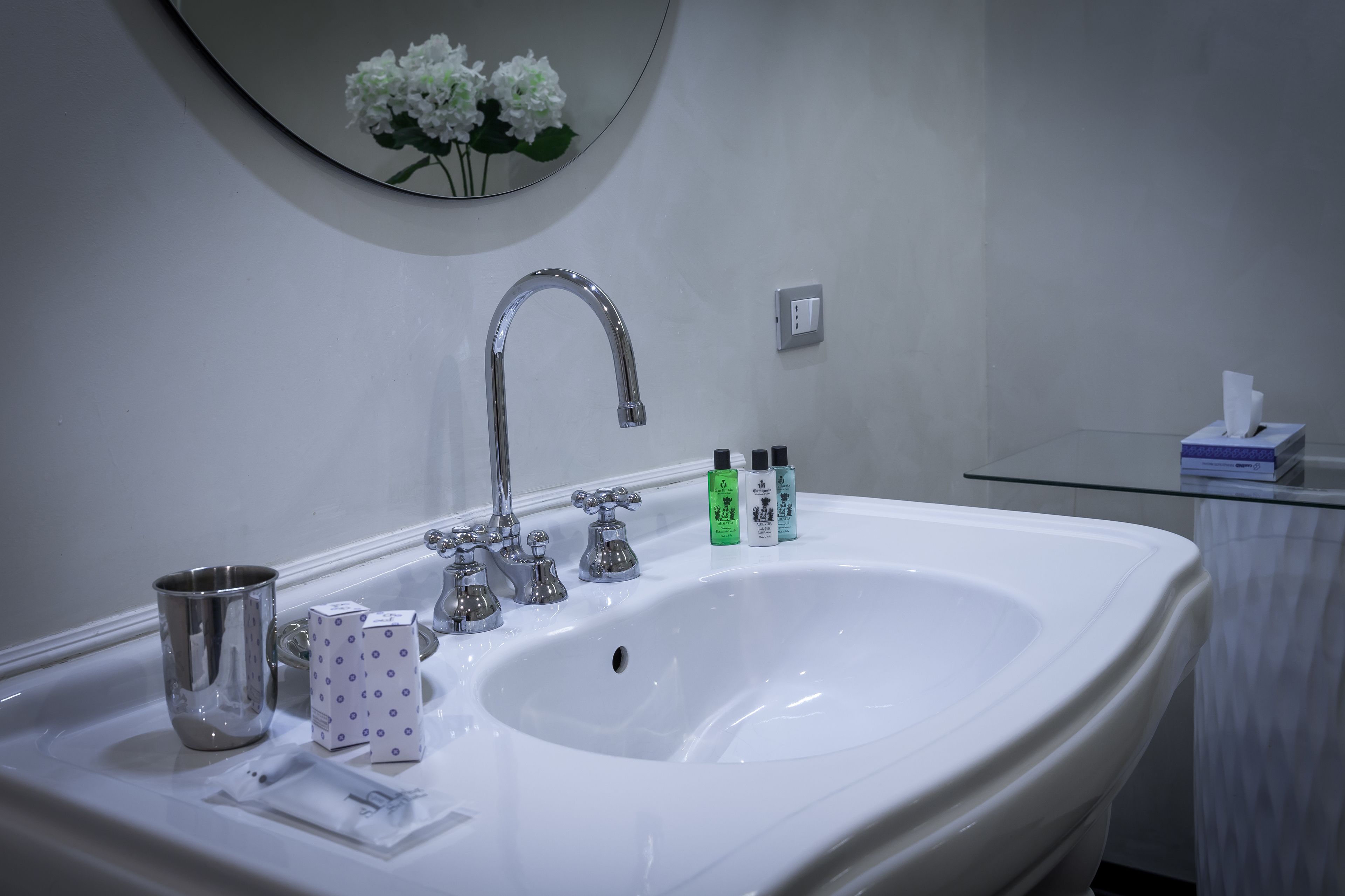 Un baño con un lavabo grande de color blanco, un espejo con decoración floral y artículos de aseo sobre el lavabo.