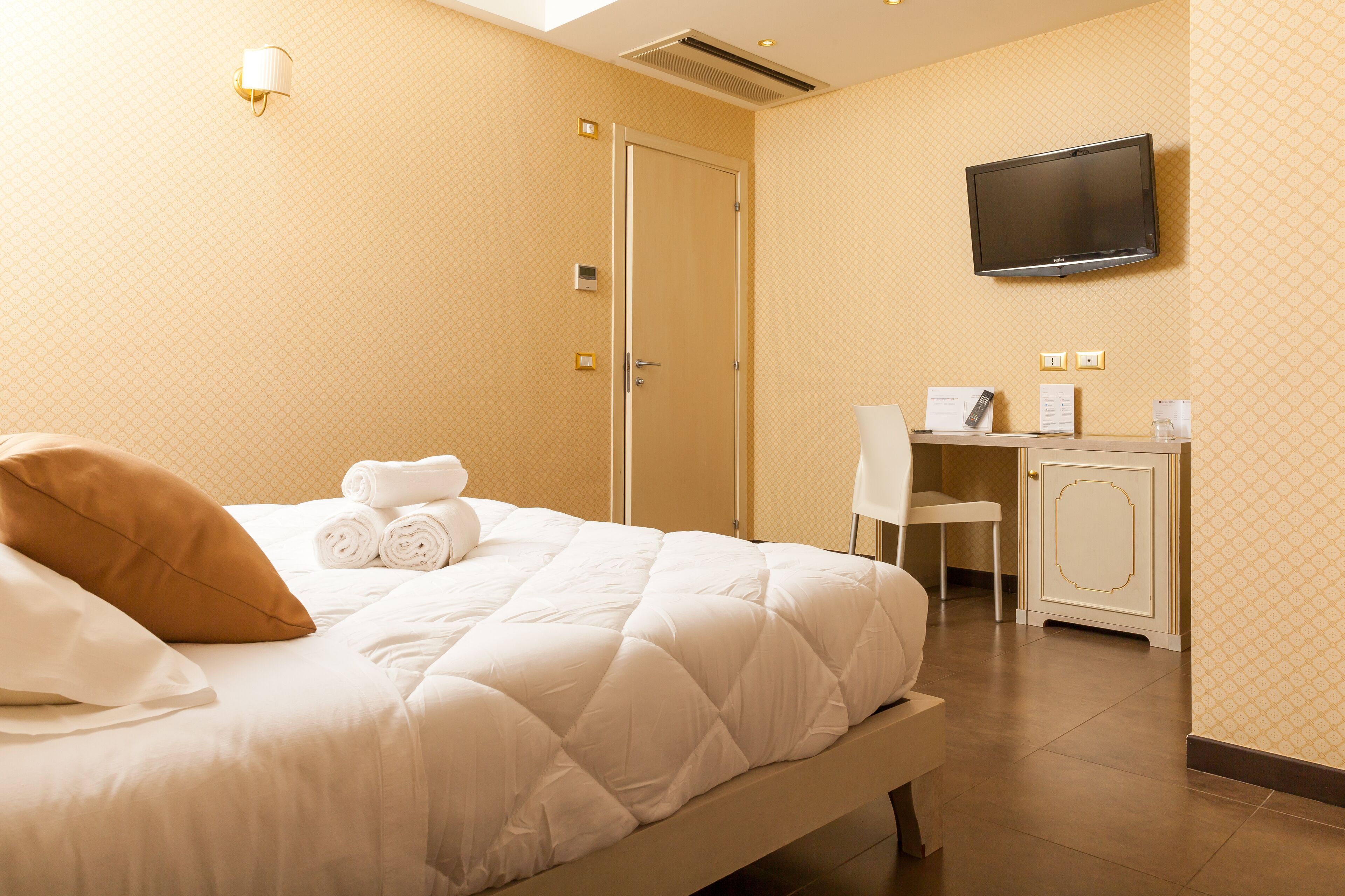 A hotel room with a bed, a desk, a television, and a door.