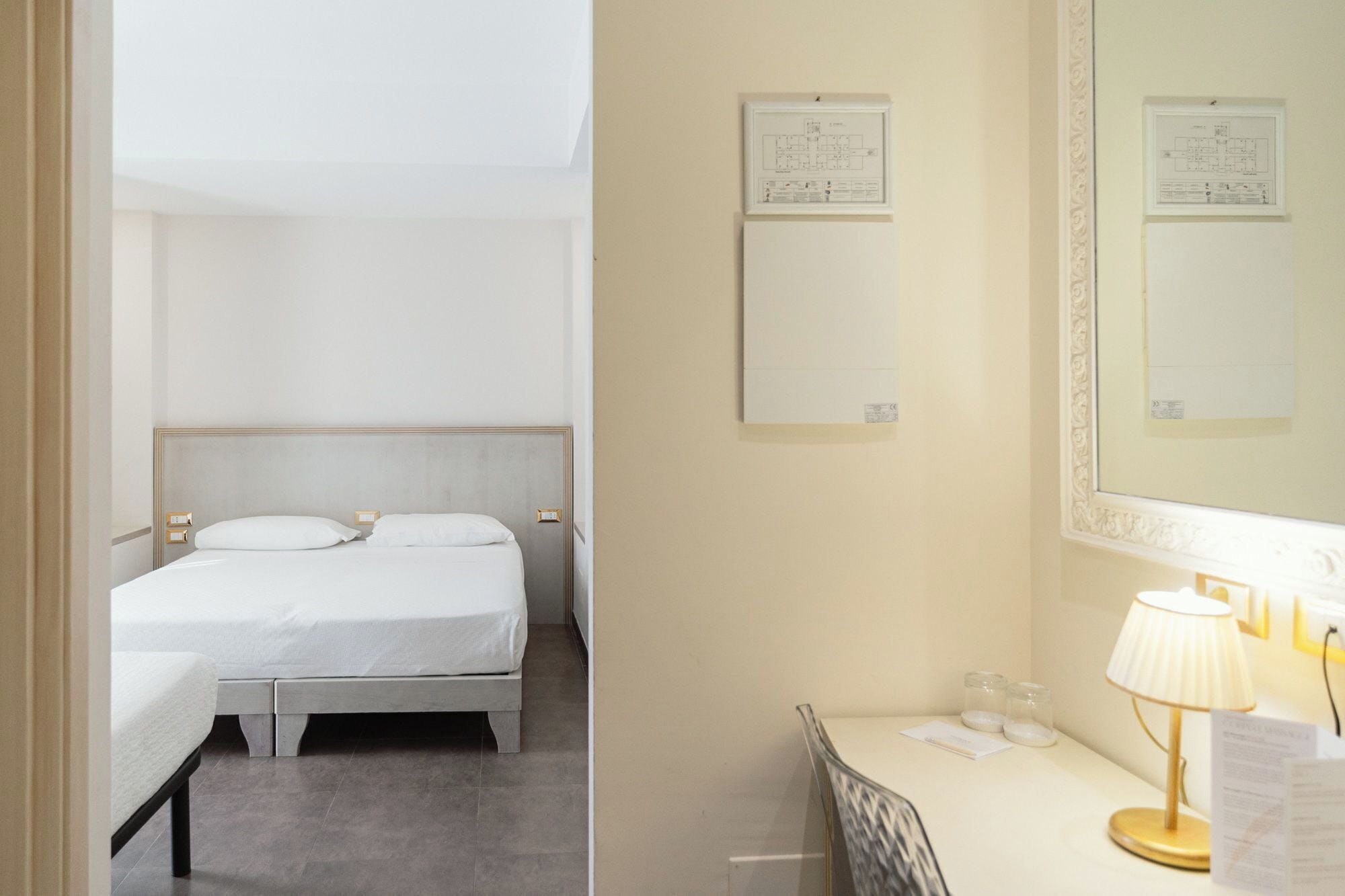 A hotel room with a bed, a bedside table with a lamp, and a mirror.