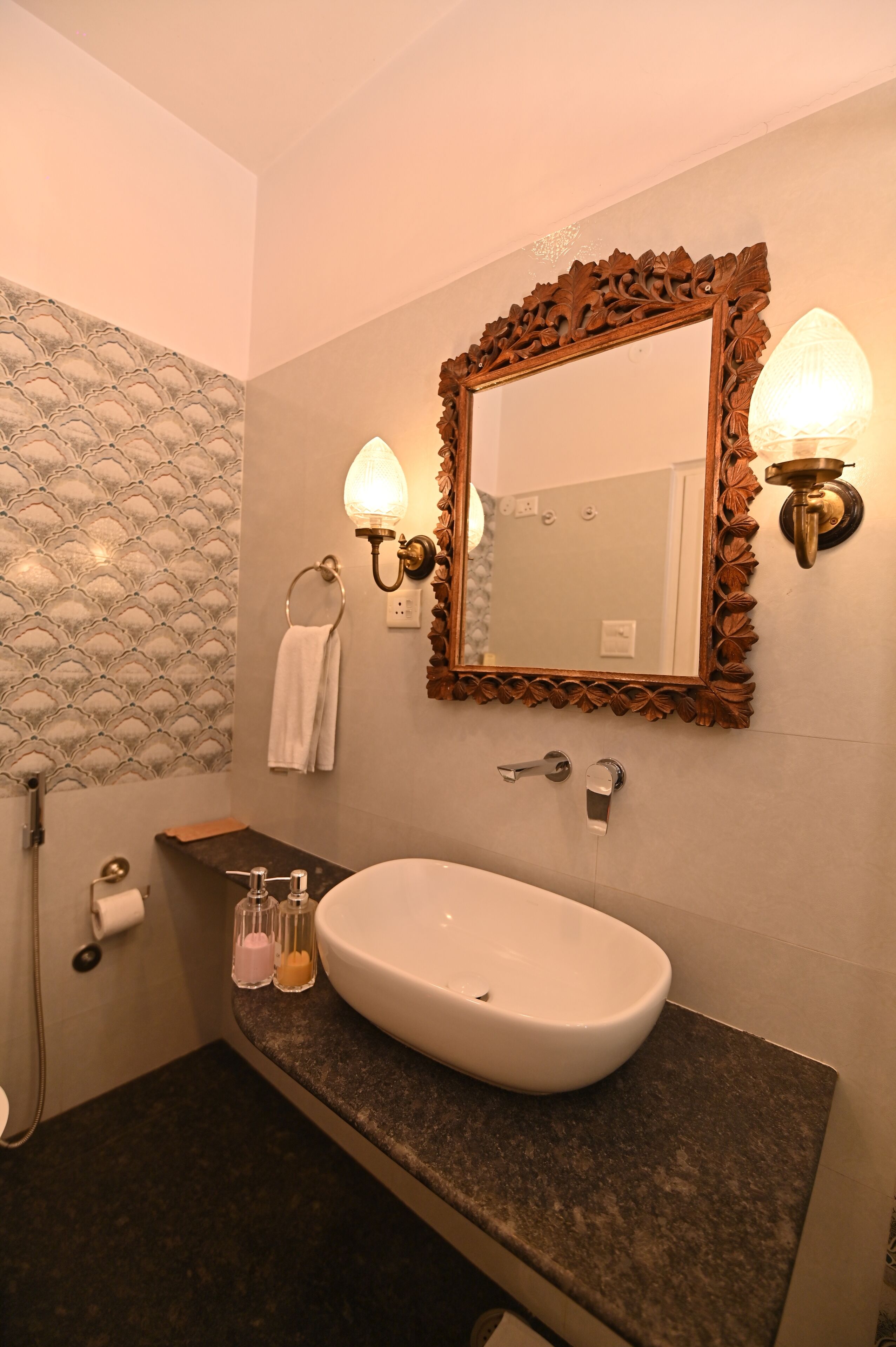 Un baño con un lavamanos blanco, un espejo con un marco decorativo y dos lámparas fijadas a la pared.