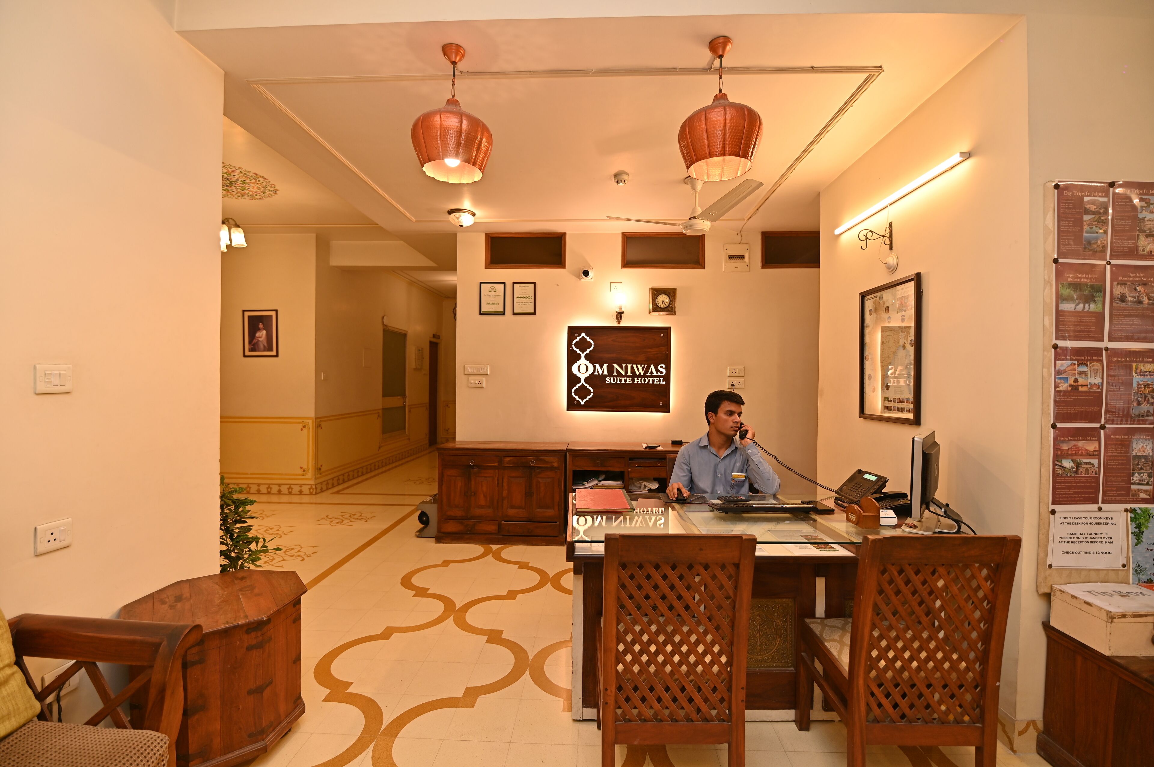 Zona de recepción de hotel con mostrador, sillas y un letrero que dice 'OM Niwas Suite Hotel'.