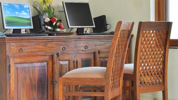 Un escritorio de madera con dos monitores, un teclado y un altavoz. Hay dos sillas de madera con respaldo trenzado.