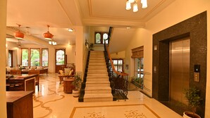 Eine geräumige Lobby mit einer imposanten Treppe, einem Empfangsbereich und einem modernen Aufzug.