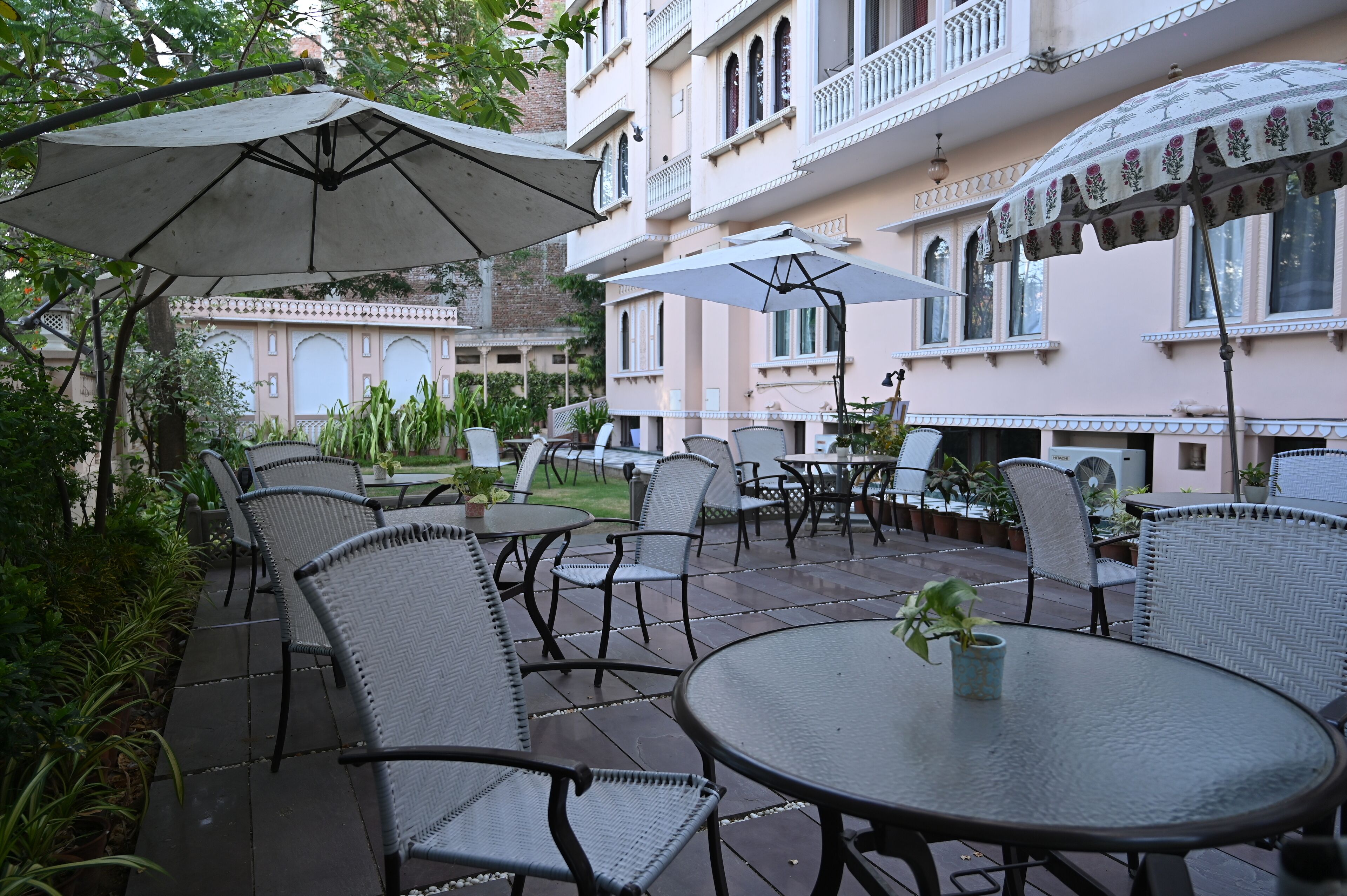 An outdoor patio area with round tables and chairs, umbrellas, and potted plants.