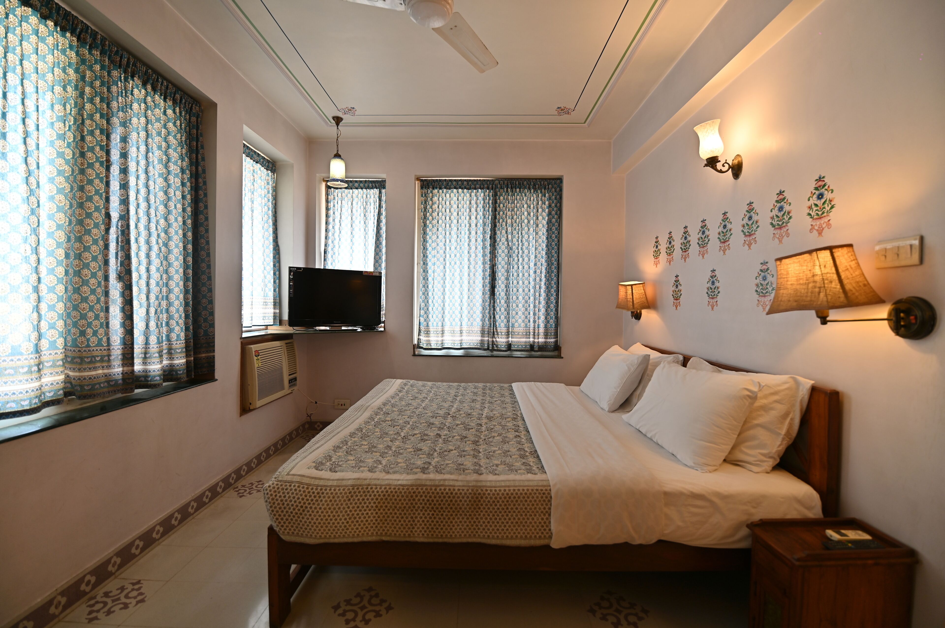 A neatly arranged bedroom with a bed, bedside lamps, a flat-screen TV, and decorative wall art.