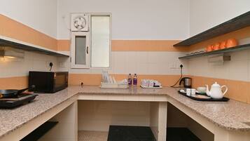 A kitchen with granite countertops, a microwave, a kettle, and orange and white tiles.