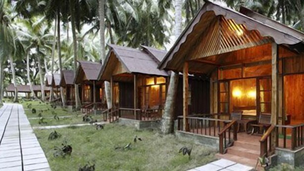 A row of wooden cabins with a porch and a wooden deck leading to them. - Symphony Palms Beach Resort (Port Blair)