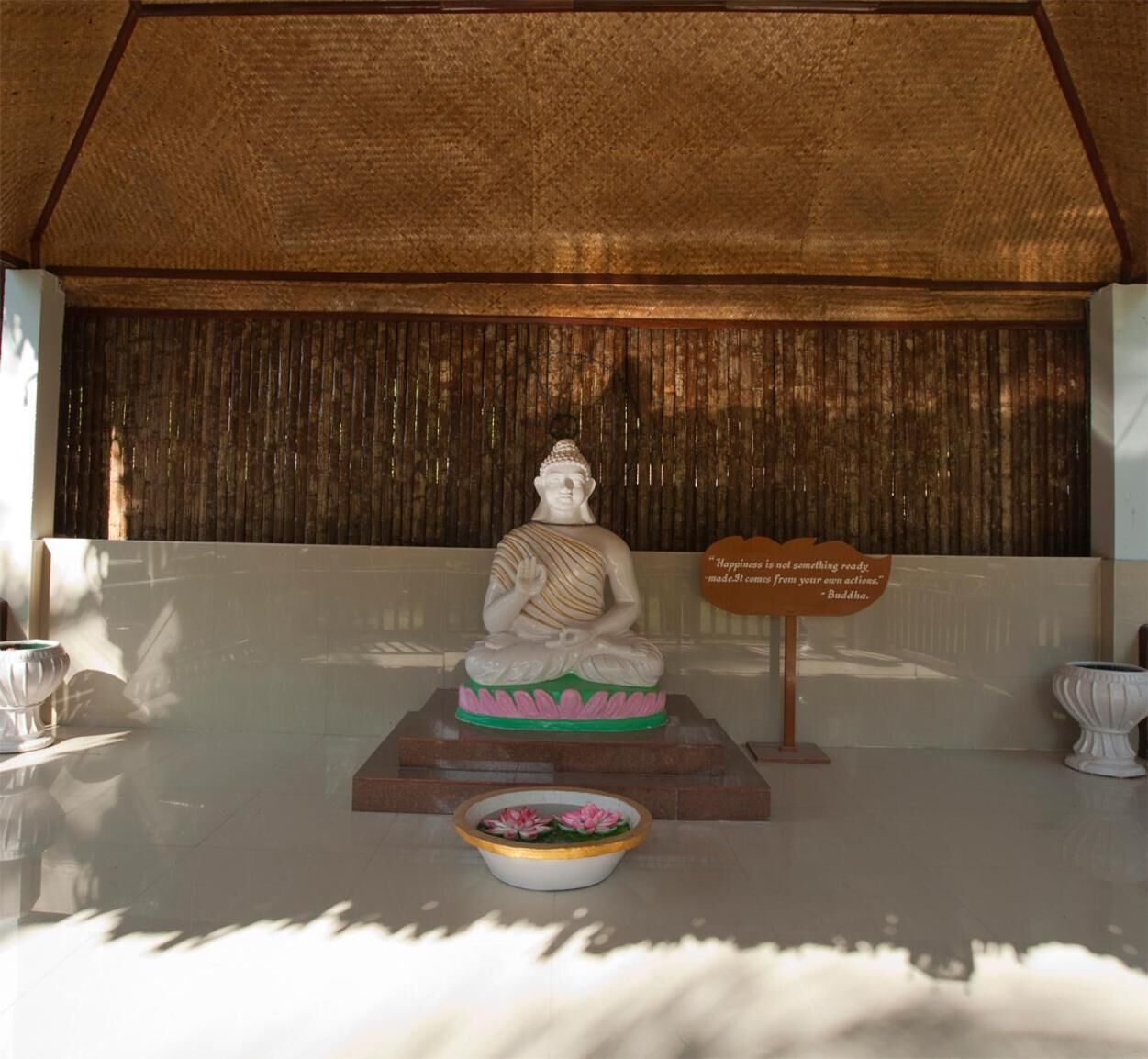 A statue of a seated figure on a pedestal with a lotus base, surrounded by a decorative bowl with flowers.