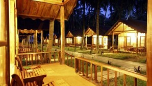 A wooden deck with outdoor seating and a view of several thatched-roof huts. - Symphony Palms Beach Resort (Port Blair)