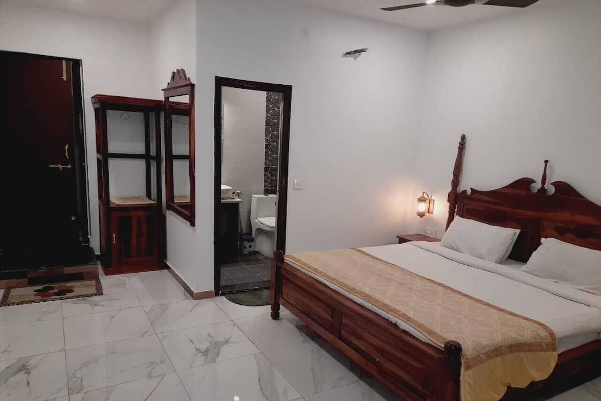Un dormitorio con cama de madera, un armario, un espejo y un baño visible a través de una puerta abierta.