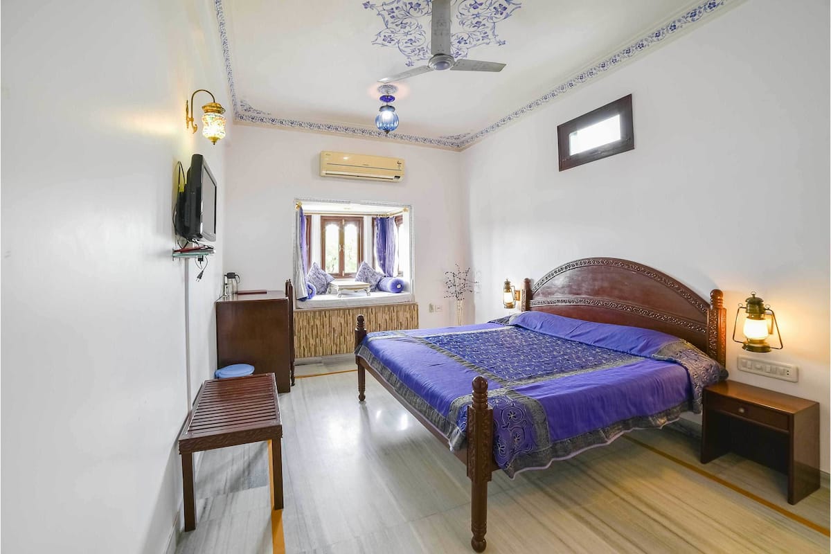 Un dormitorio con una cama de madera, un escritorio, una silla, un ventilador de techo y una ventana con cortinas.
