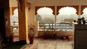 Una habitación con suelo de baldosas, plantas en macetas, una silla y vistas a través de una ventana con arcos decorativos.