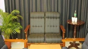 A room with a sofa set, a small round table with a bottle and glasses, and a potted plant.