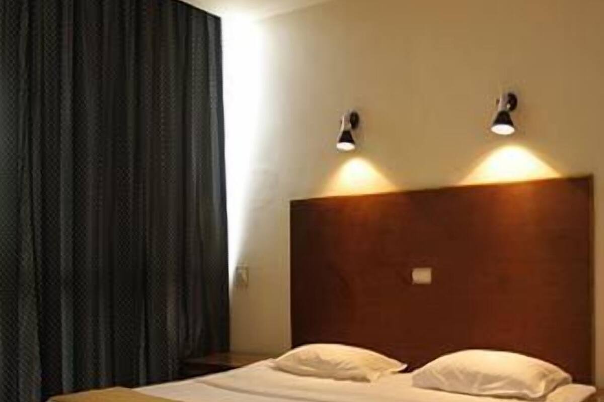 A hotel room with a wooden bed, two bedside lamps, and a dark curtain.
