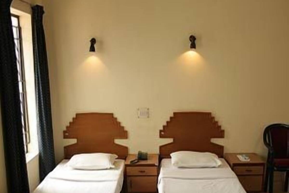 A hotel room with two single beds, a nightstand between them, and a chair.