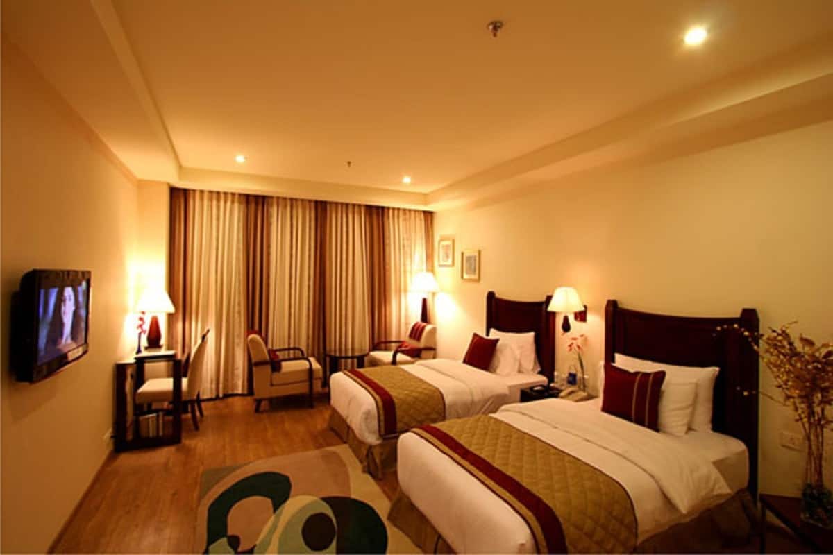 Ein Hotelzimmer mit zwei Betten, einem Fernseher, einem Schreibtisch und einem Sessel.