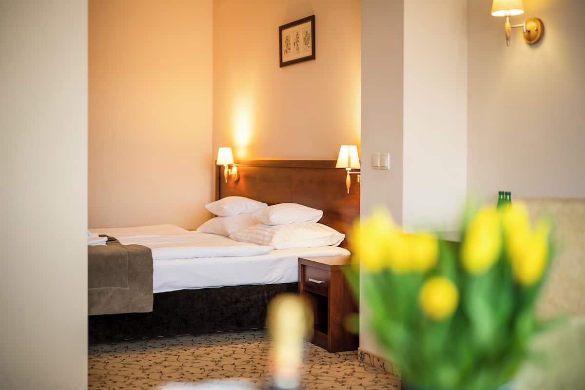A hotel room with a bed, bedside lamps, a nightstand, a framed picture on the wall, and a vase with flowers.