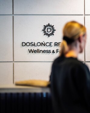 A sign with the text 'DOSLONCE RE' and a logo, with a person walking in the background. - Dosłońce Resort Wellness & Farm (Raclawice)