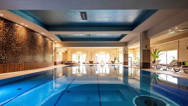 A large indoor swimming pool with clear lanes, a tiled wall, and lounge chairs along the side. - Dosłońce Resort Wellness & Farm (Raclawice)