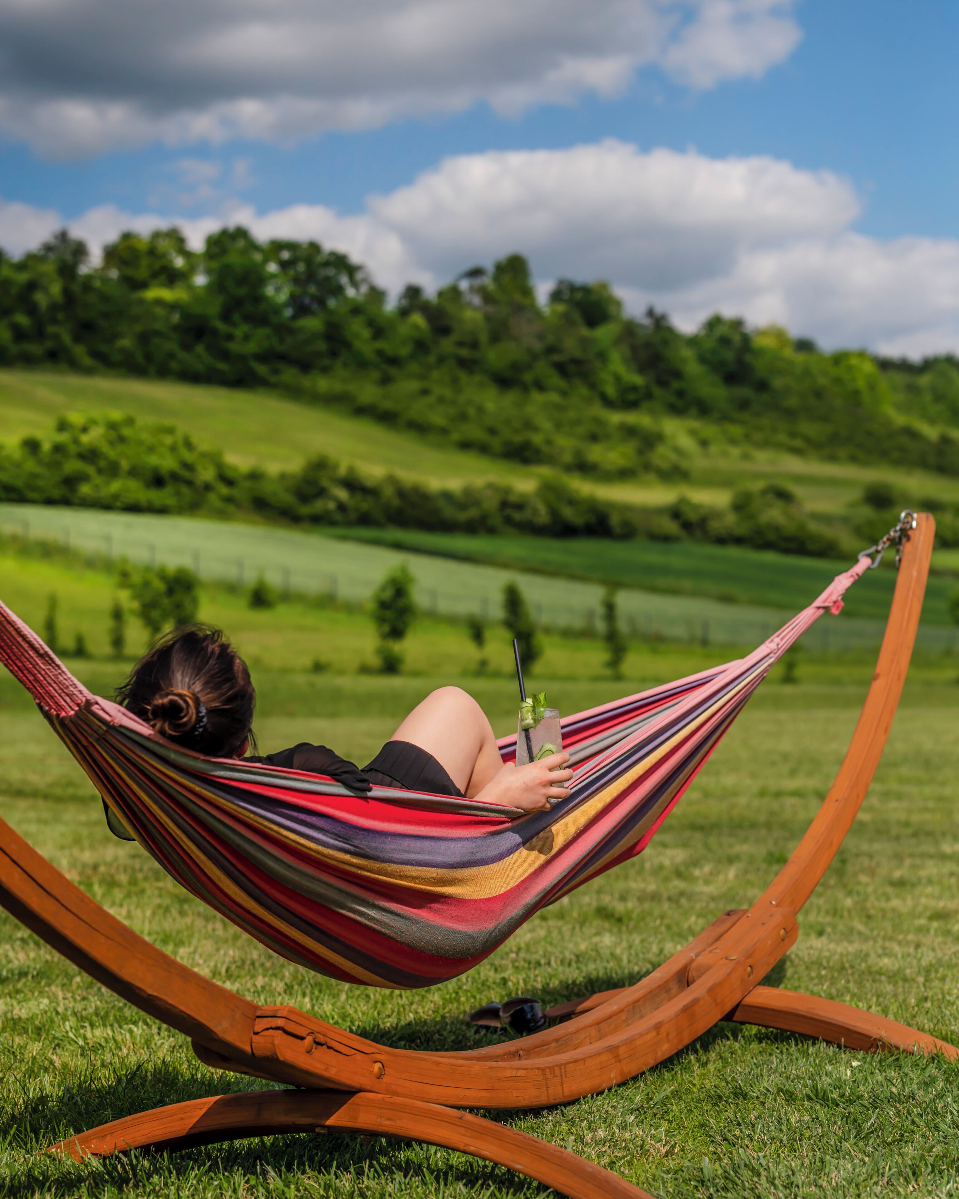 A person relaxing in a hammock on grass with a view of a green landscape.
