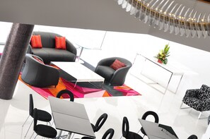 A modern lounge area with a black sofa set, a glass coffee table, and a patterned rug. There are black chairs around the table, and a small plant on a white stand. - Quest Canberra Dickson (Dickson)