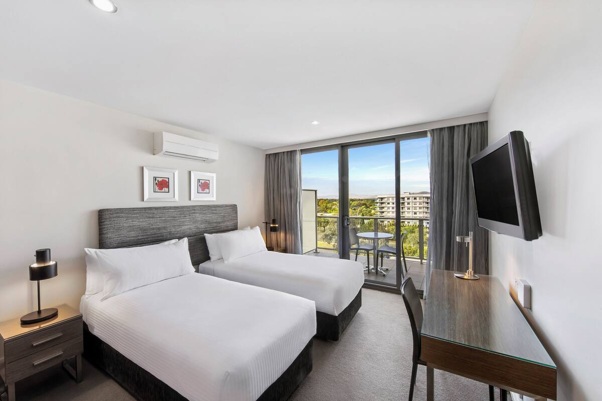 Ein Hotelzimmer mit zwei Betten, einem Schreibtisch, einem Fernseher und einem Balkon mit Aussicht.