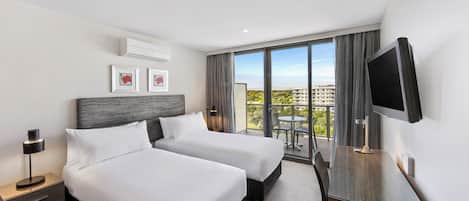 A hotel room with two beds, a desk, a TV, and a balcony with a view.