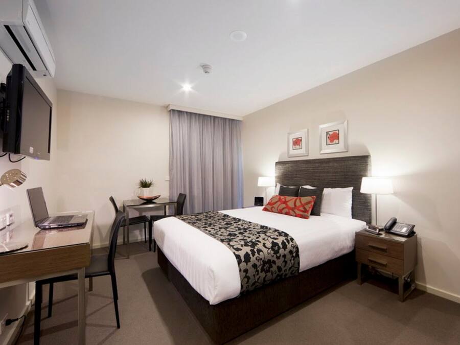Hotelkamer met een bed, nachtkastje, lamp, bureau met laptop, stoel en een aan de muur bevestigde televisie.