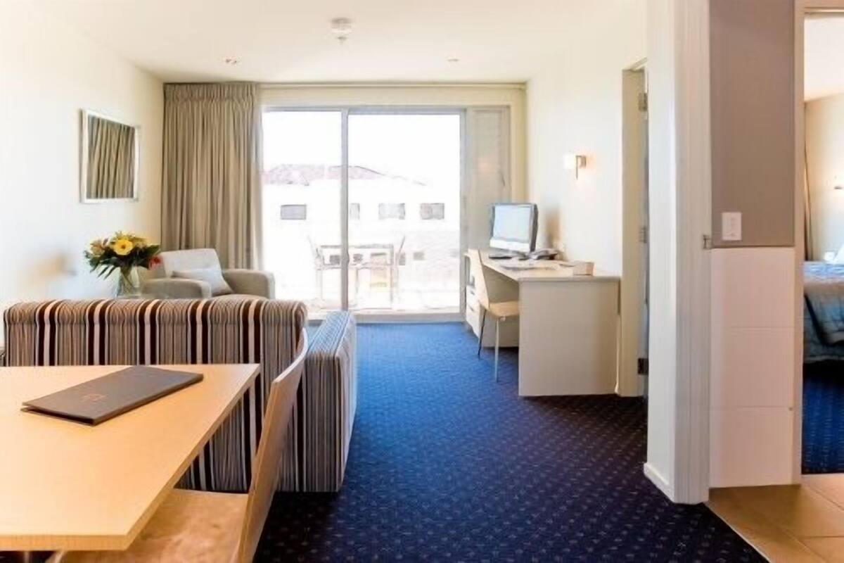 A hotel room with a sofa, a small table, a desk with a computer, and a view of the outside.