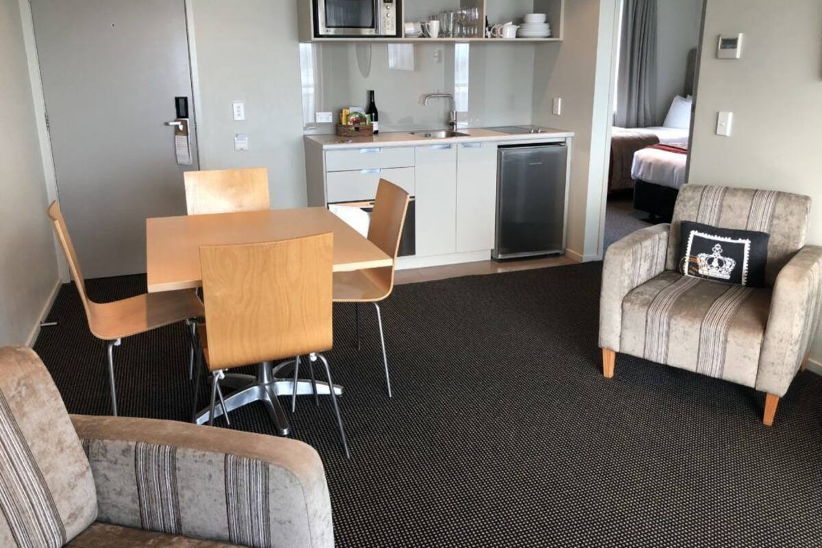 A compact hotel room with a kitchenette, a dining area with a table and chairs, and a seating area with a sofa and armchair.