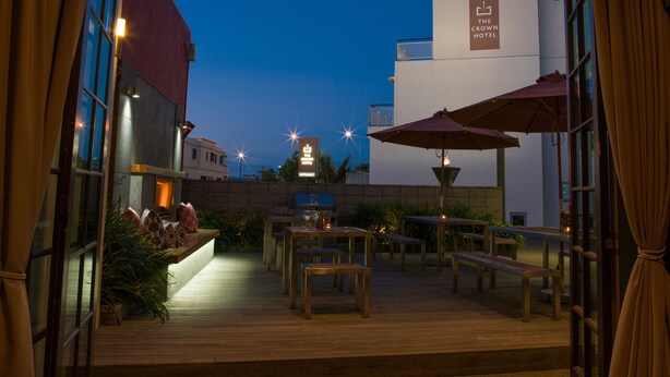 Un patio al aire libre con mesas y bancos de madera, un cartel para The Crown Hotel y vistas del edificio del hotel.