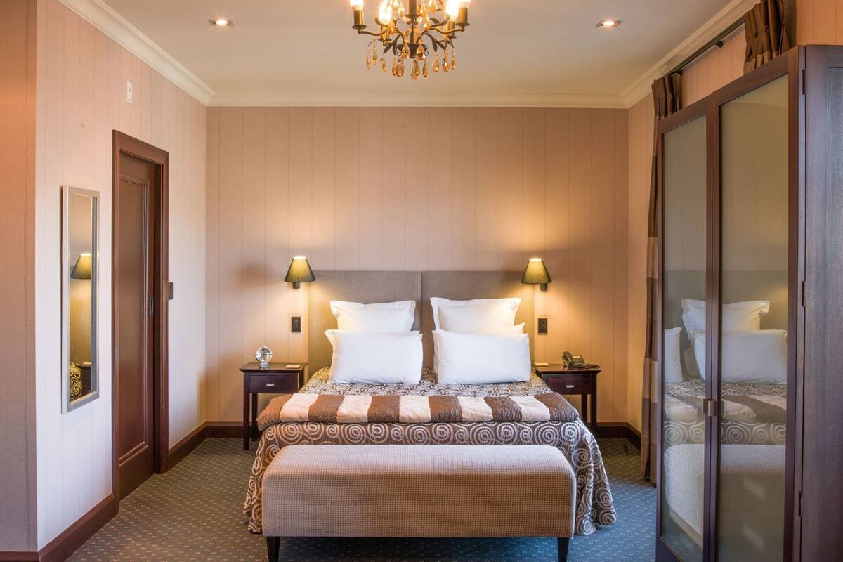 A hotel room with a large bed, two bedside tables, a chandelier, and a sliding glass door.