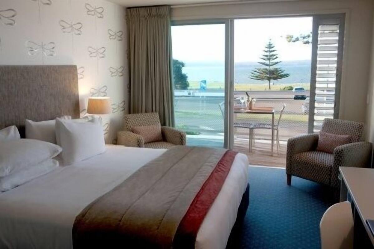 A hotel room with a large bed, two chairs, a table, and a view of the outdoors.