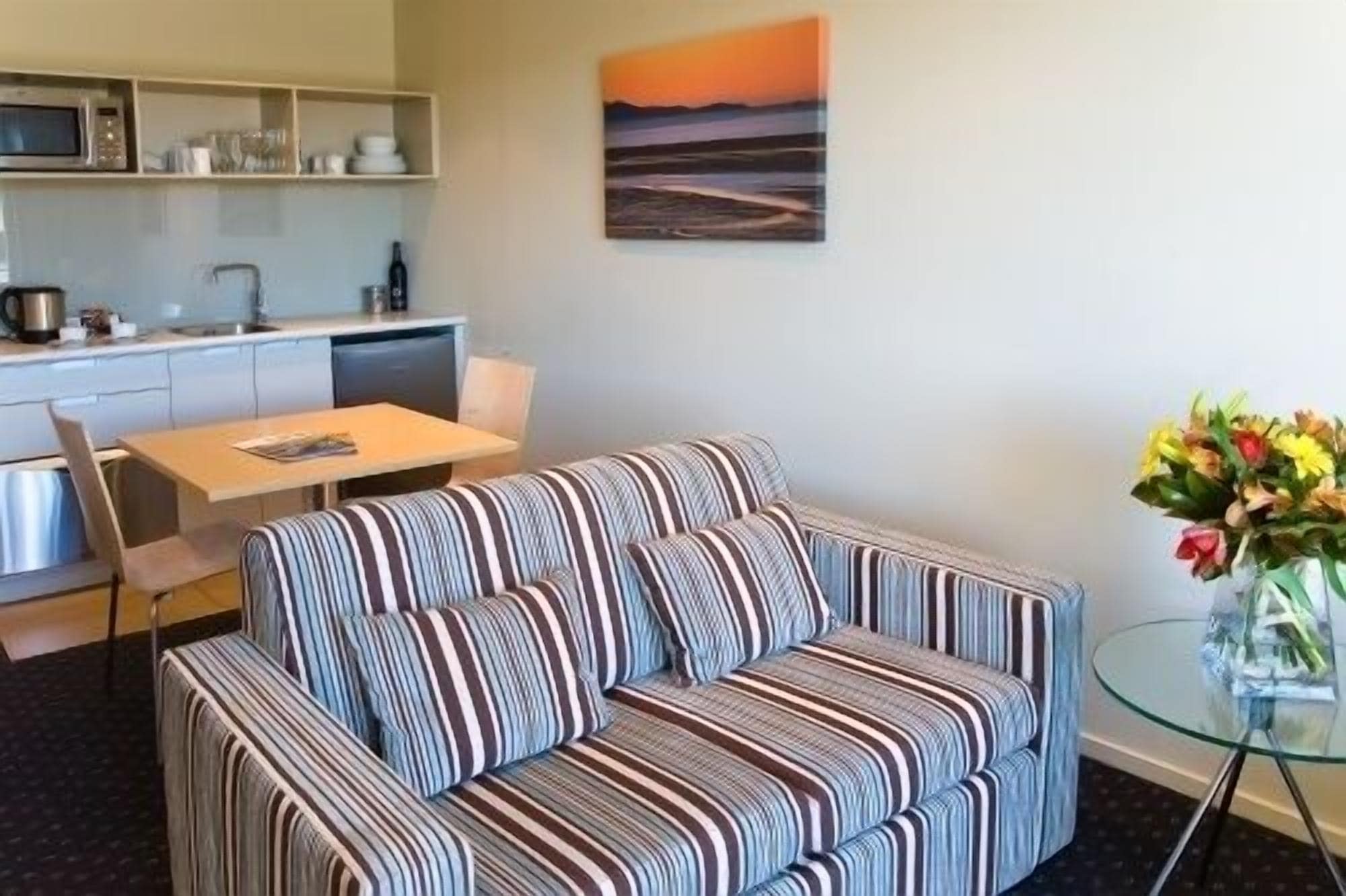 A living area with a striped sofa, a dining table, and a kitchen in the background.