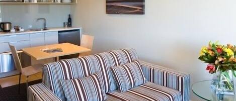 Un espacio habitable con un sofá a rayas, una mesa de comedor y una cocina al fondo.