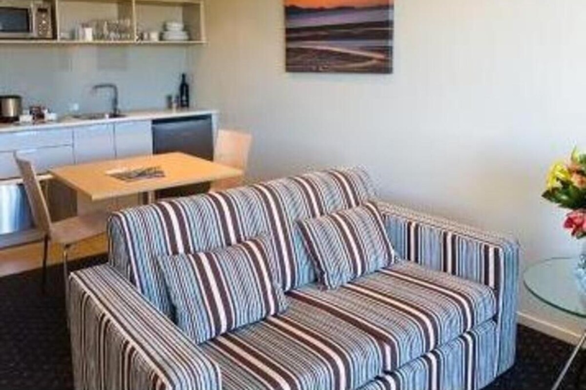 A modern living room with a striped sofa, a dining table, and a kitchen area with built-in appliances.