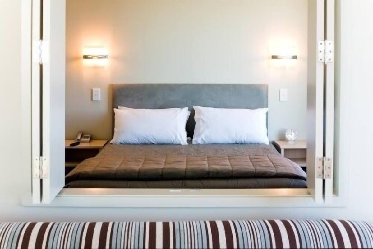 A bed with a headboard, two bedside tables, and wall-mounted lights.